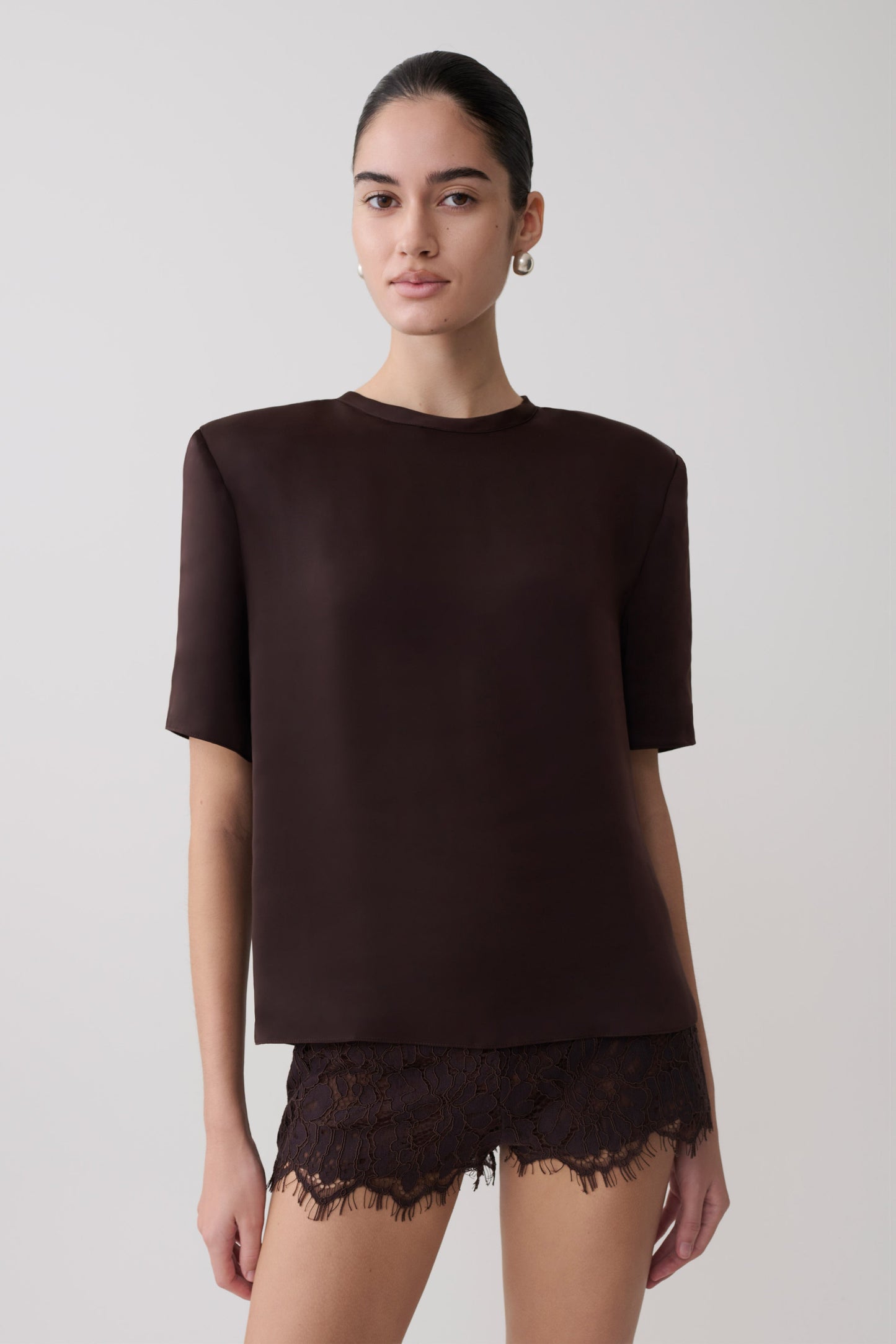 Woman wearing a dark brown shoulder pad short sleeve satin top with matching lace shorts.