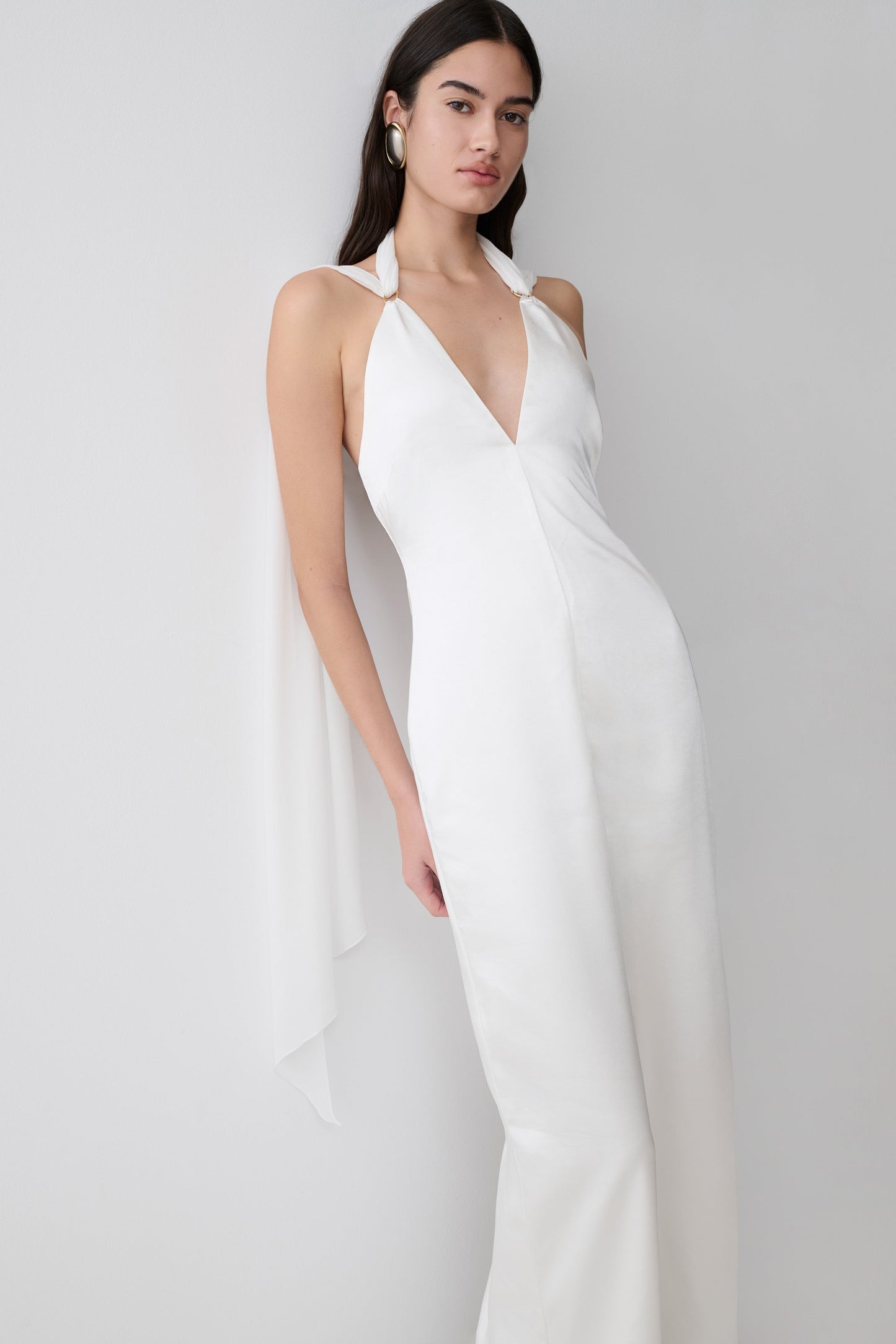 Woman wearing a white satin maxi dress with draped shoulders.
