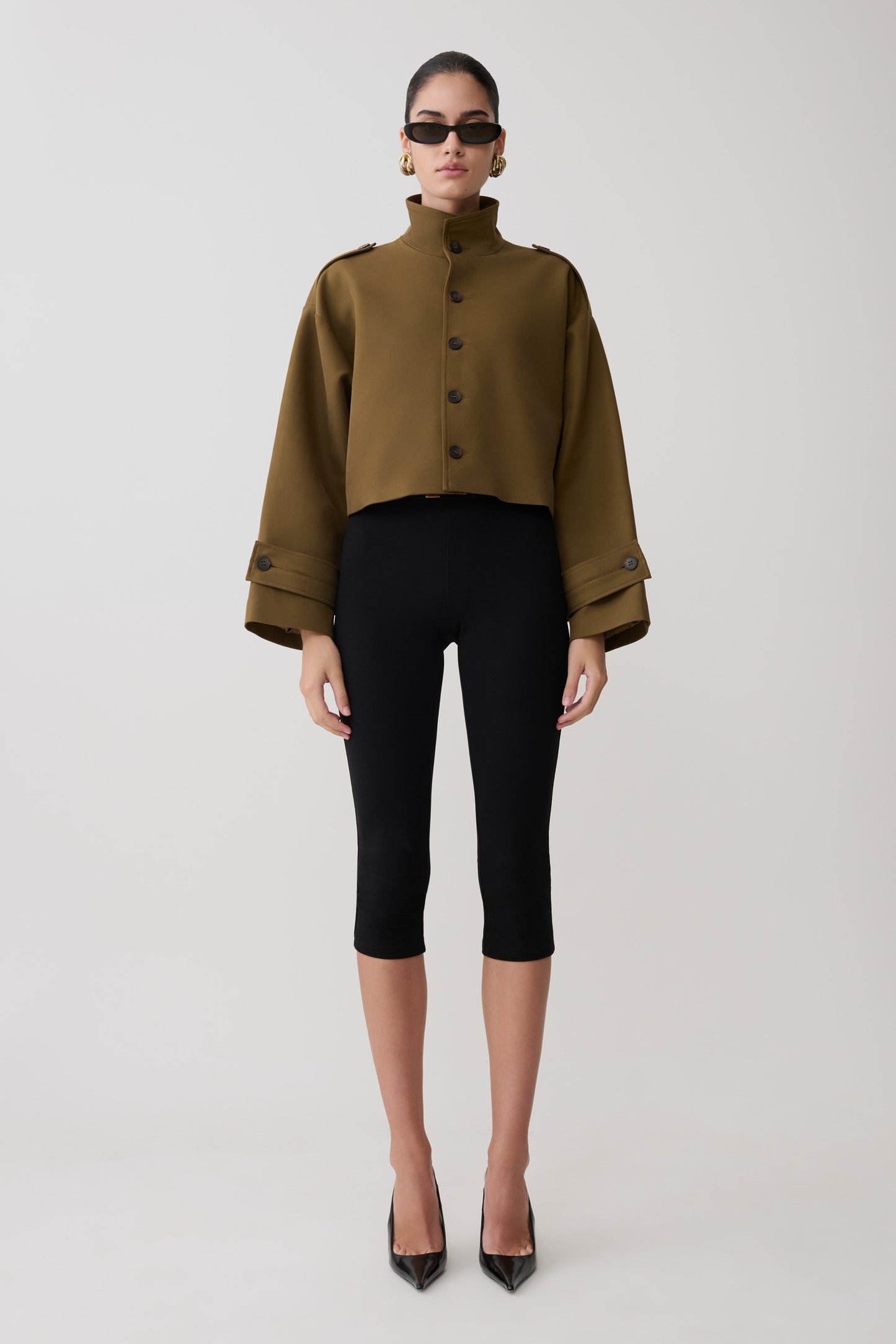 Woman wearing a khaki jacket and black pants on a white background.