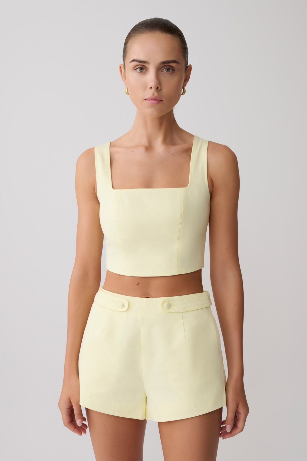 Woman wearing a light yellow sleeveless top and matching shorts.