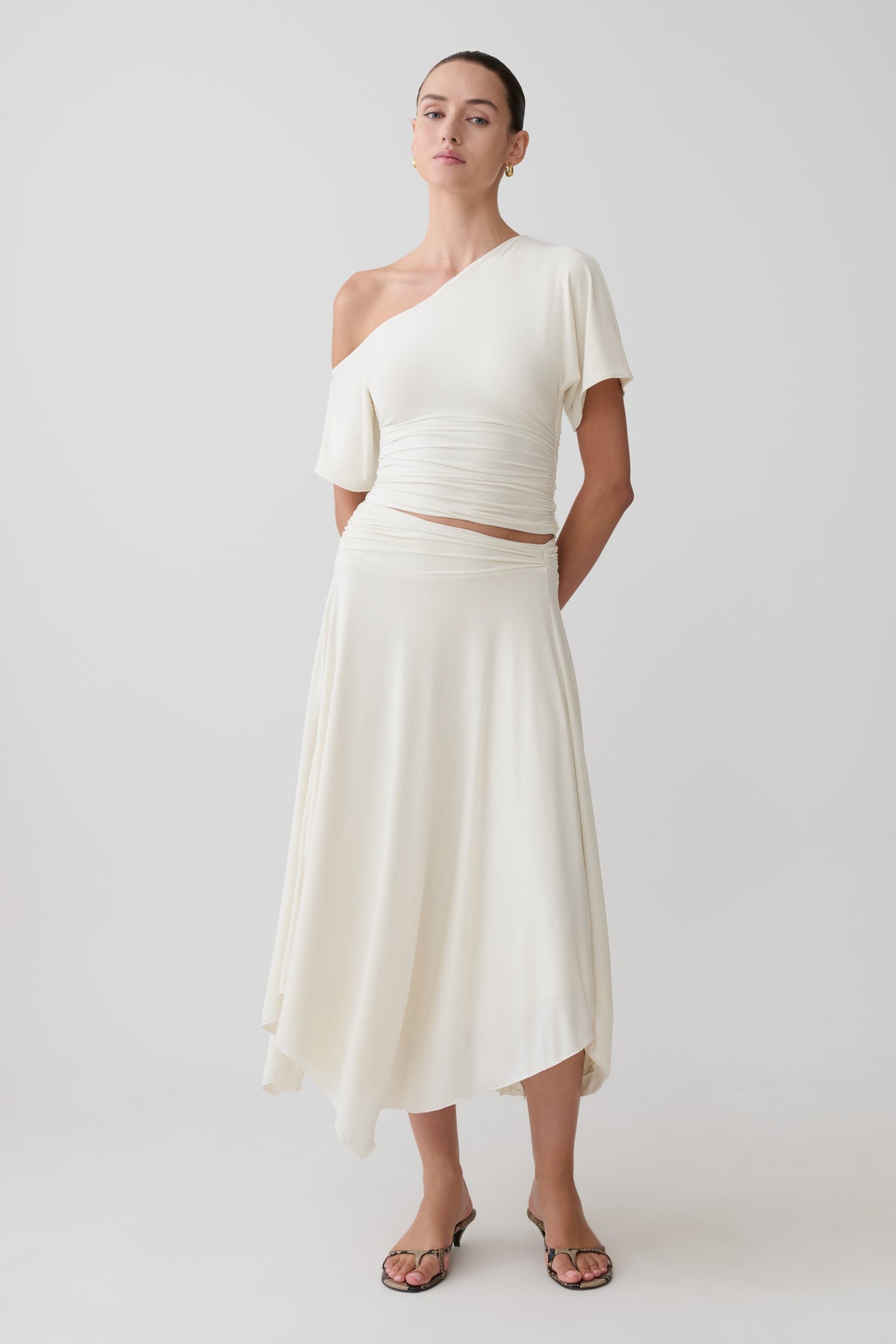 Woman wearing a white one-shoulder top with a matching midi skirt.