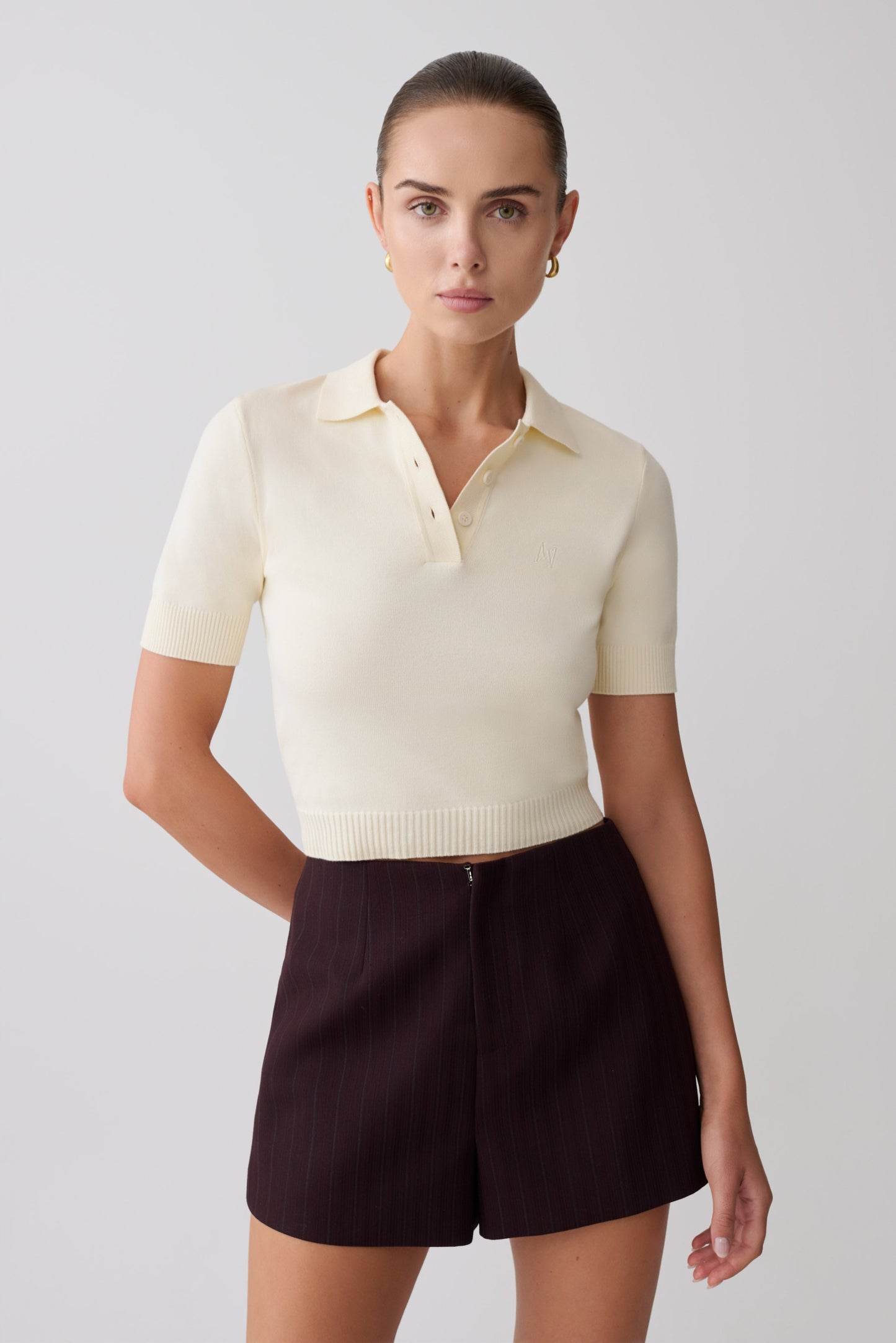 Woman wearing a cream-colored polo shirt and dark brown shorts.