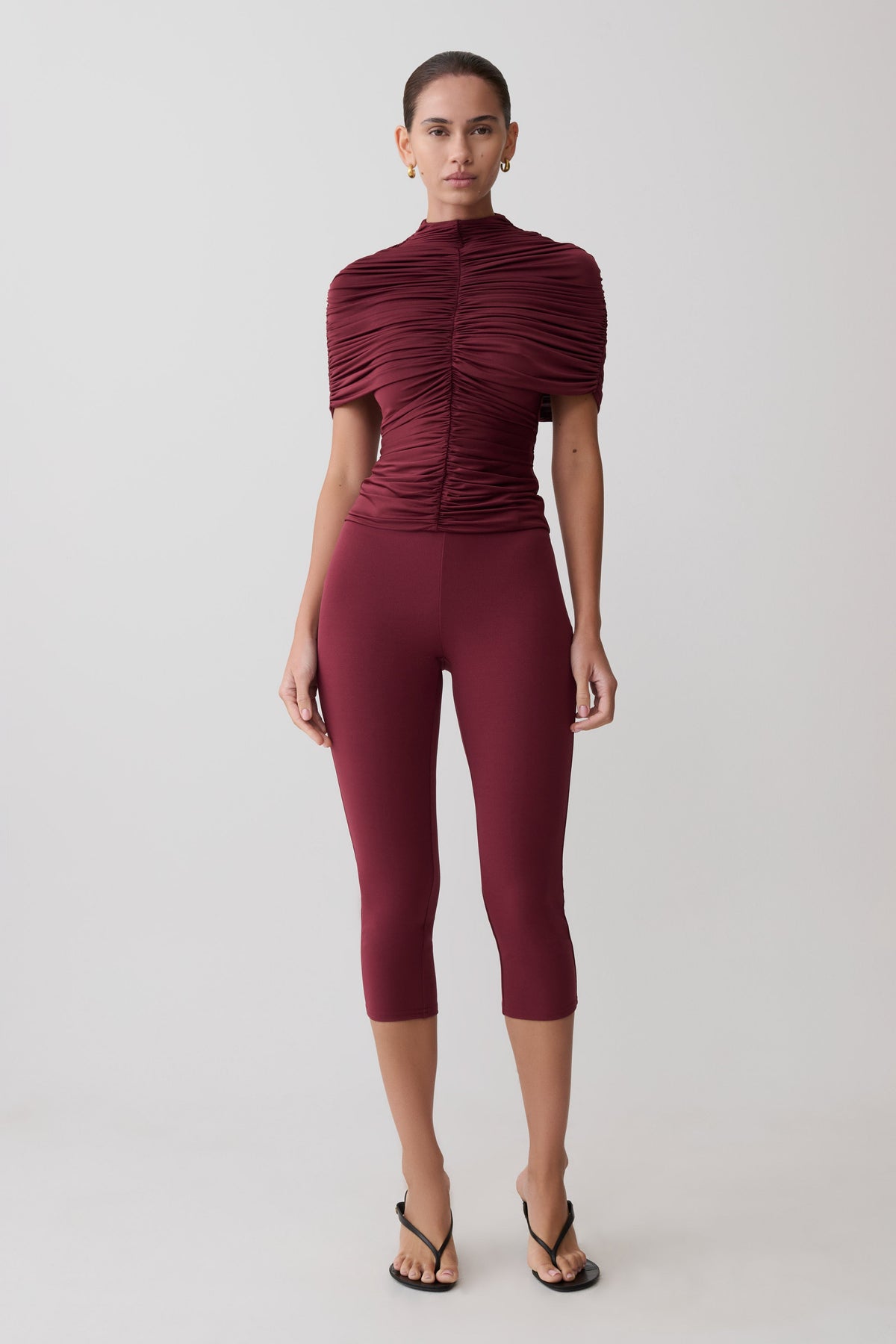 Woman wearing a burgundy ruched top and leggings on a white background
