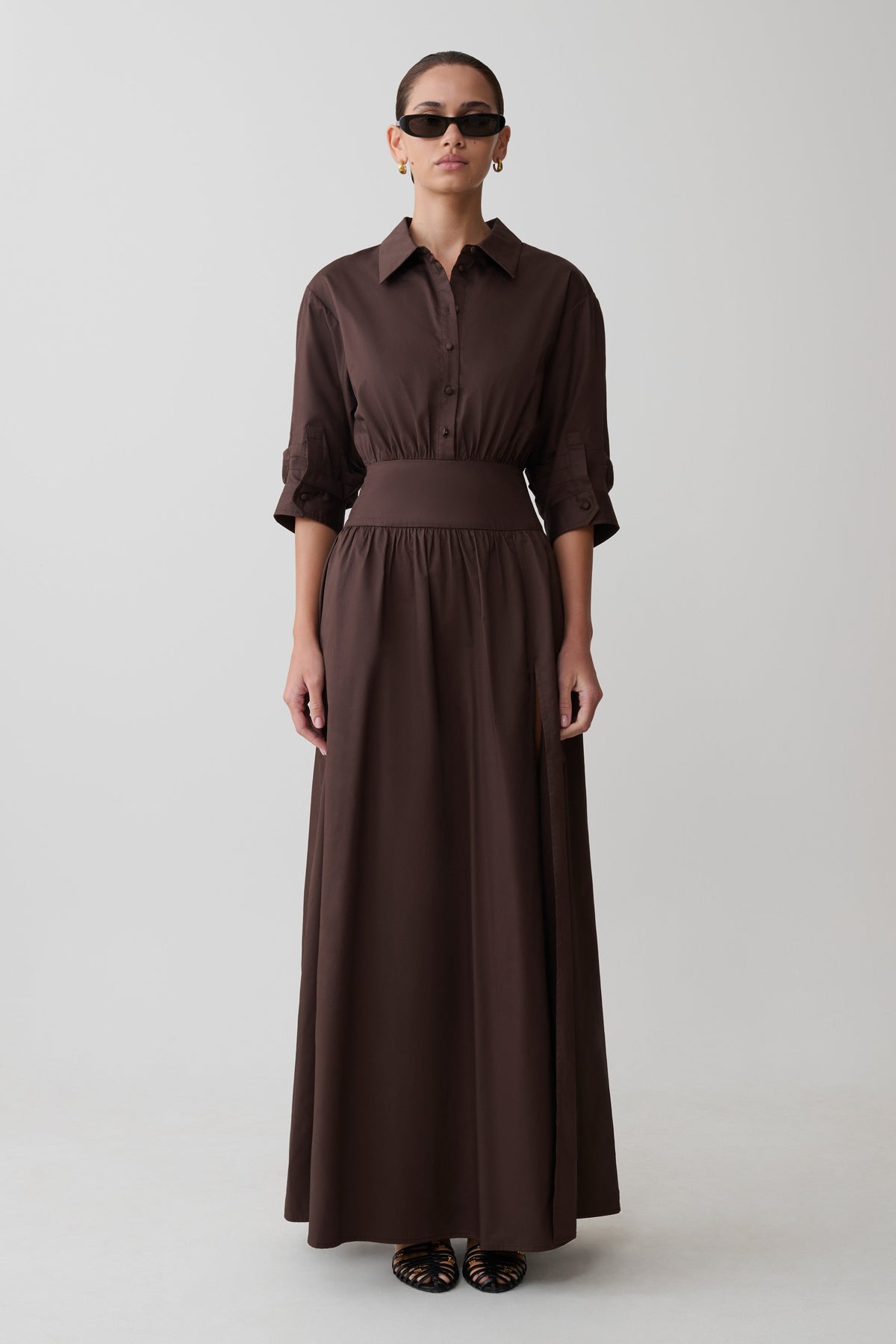 Woman wearing a long brown dress with a belt on a white background