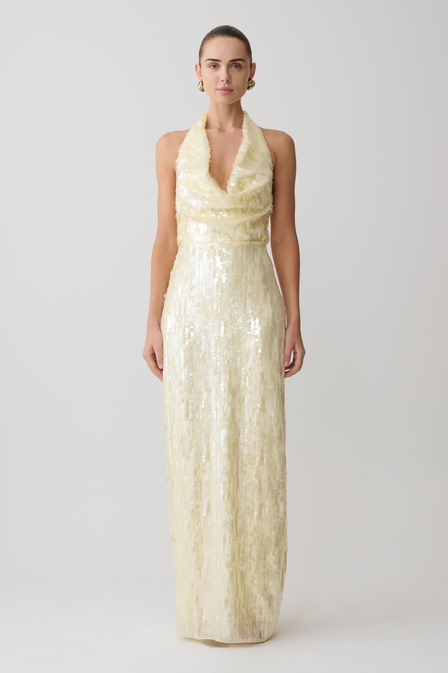 Woman wearing a long, light-colored sequin dress on a white background