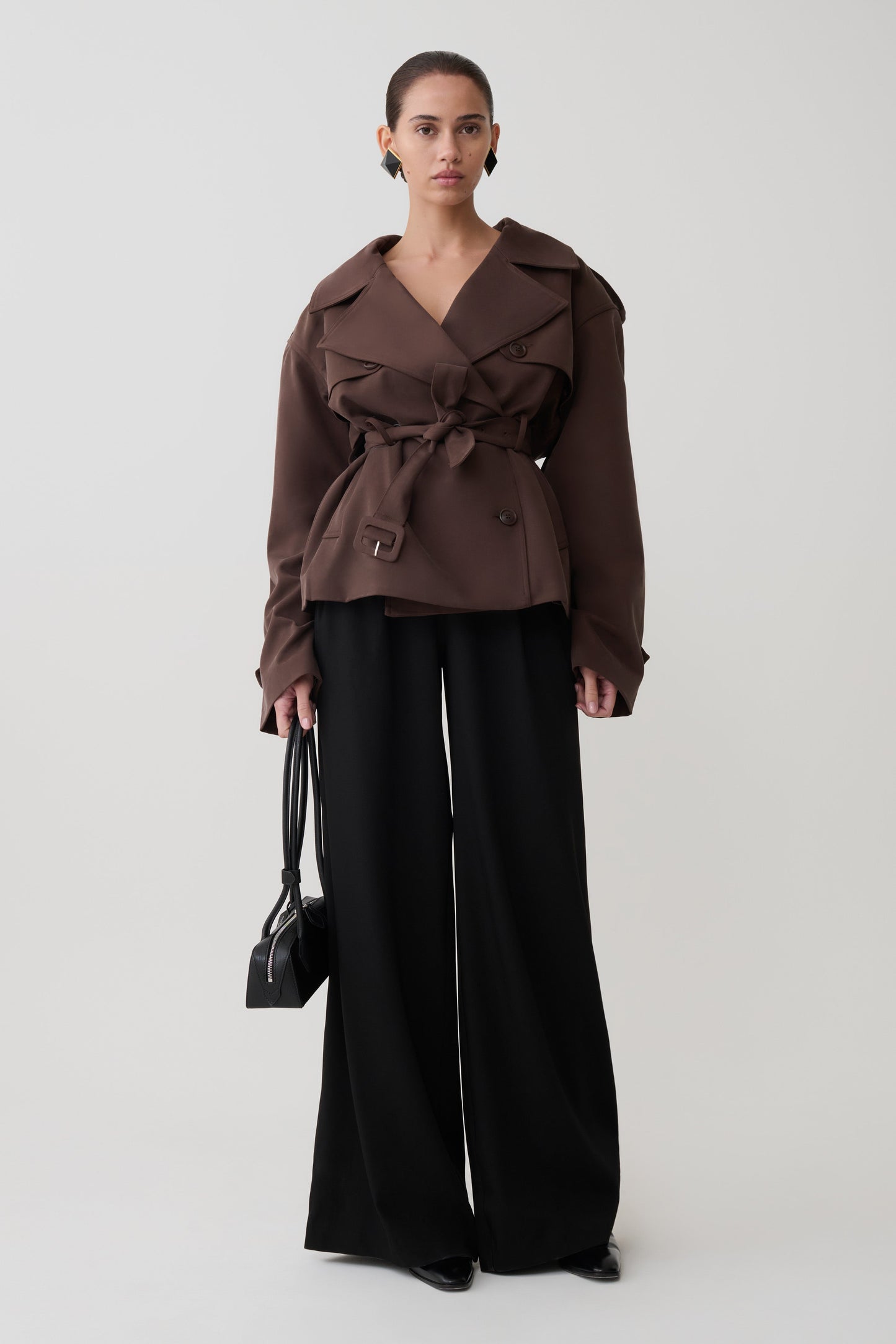 Woman wearing a brown trench coat and black pants on a white background