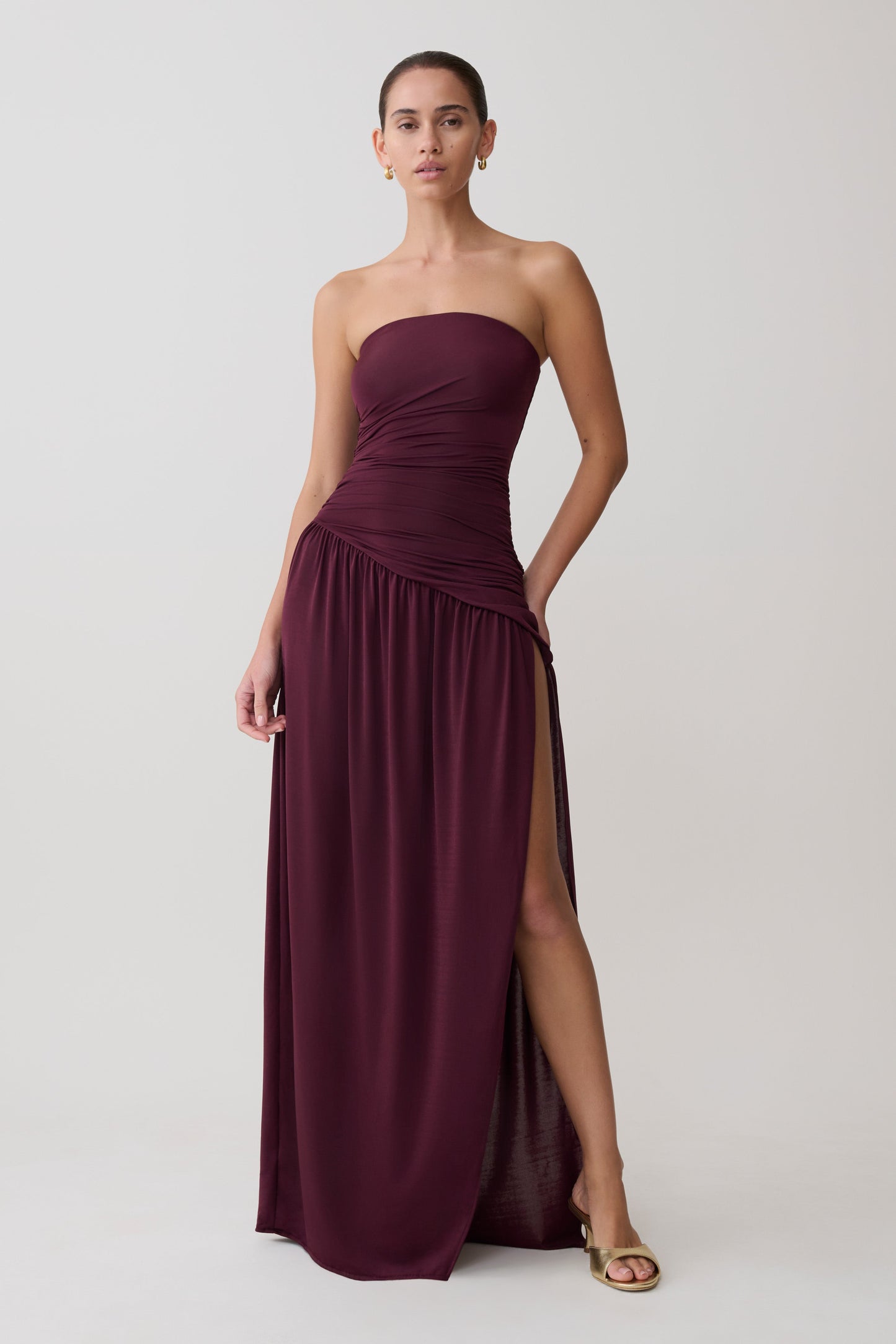Woman wearing a strapless burgundy gown with a slit on a white background