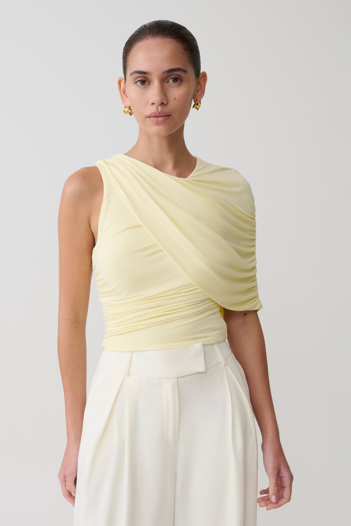Woman wearing a light yellow top and white pants on a plain background