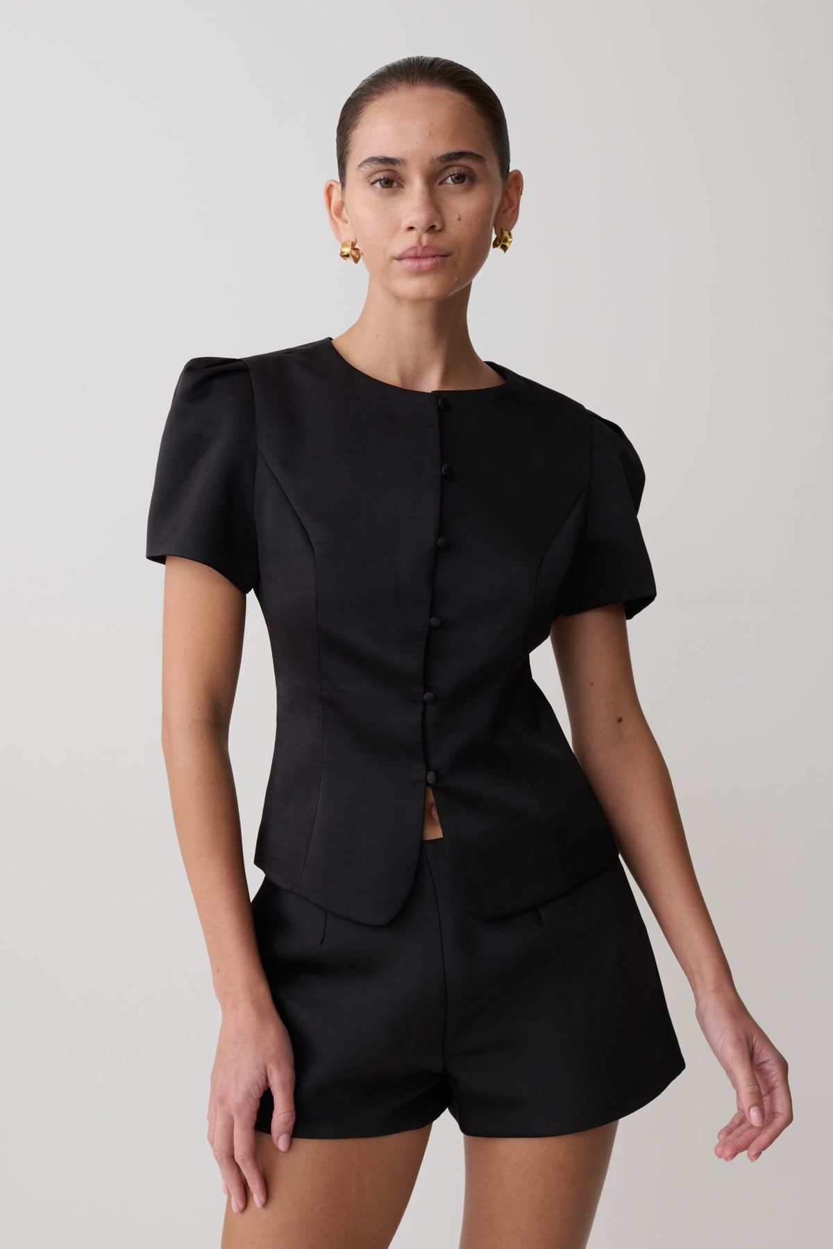 Woman wearing a black outfit with puffed sleeves on a plain background