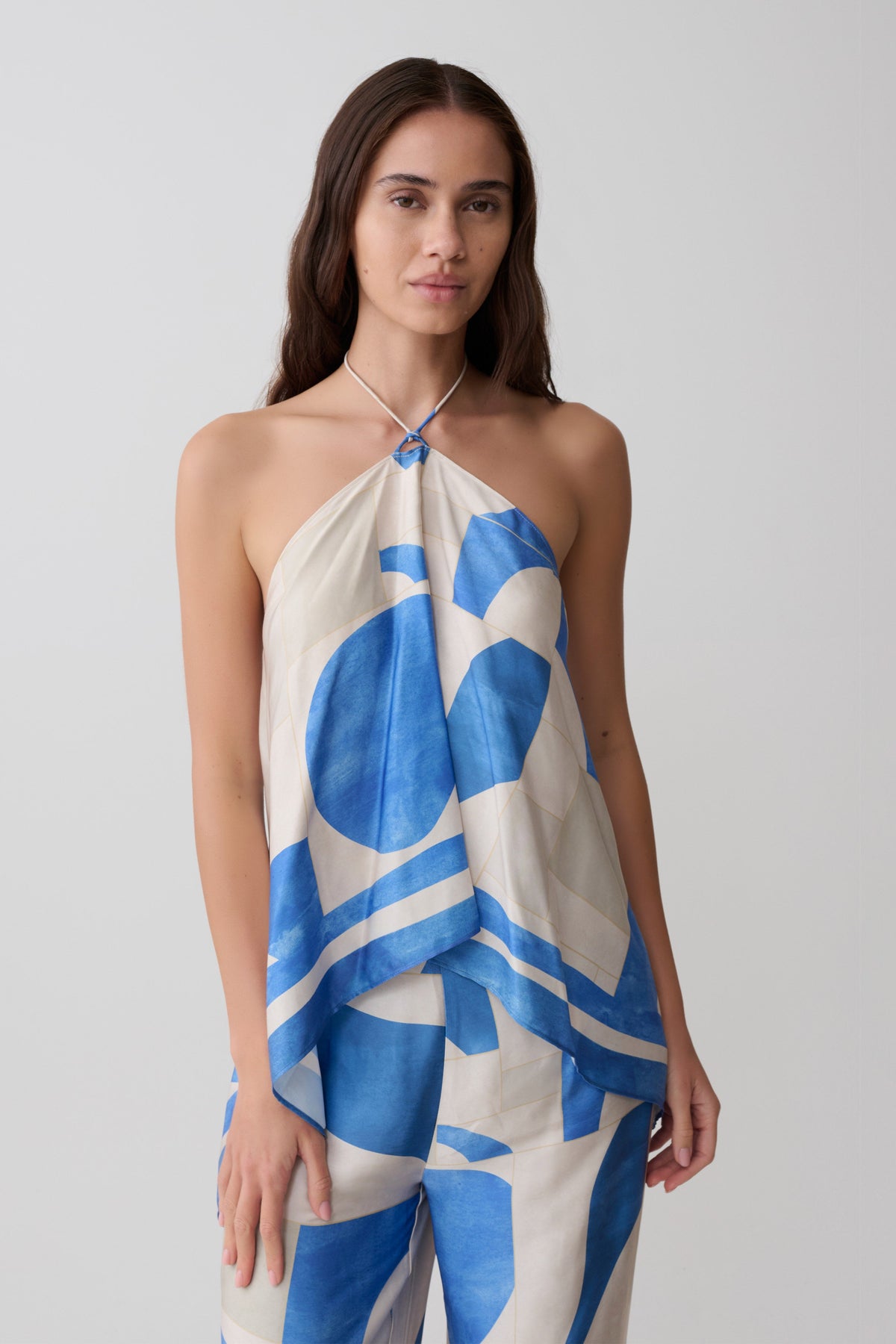 Woman wearing a blue geo tiled draped satin halter top.