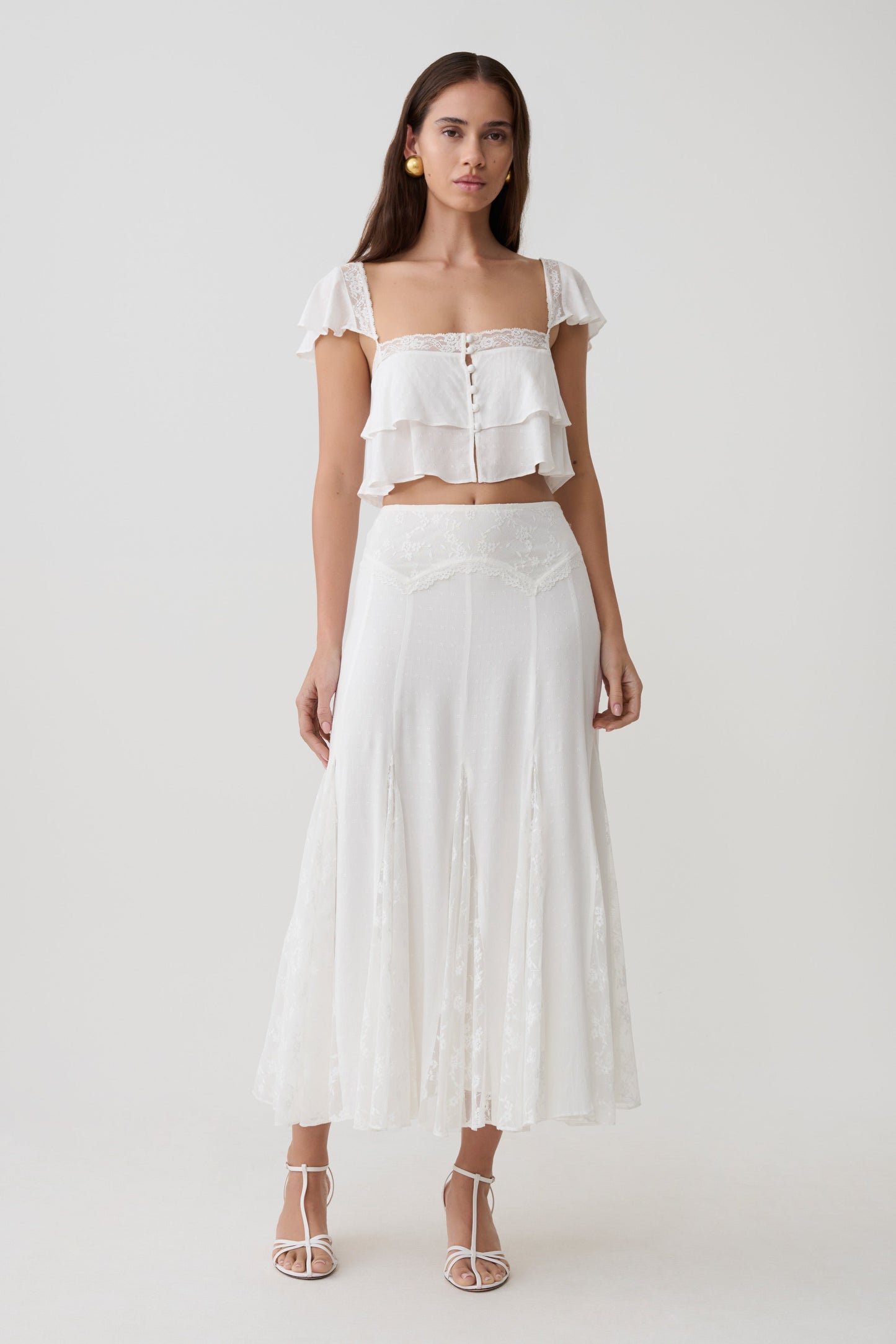 Woman wearing a white lace sleeveless crop top with matching panelled midi skirt.