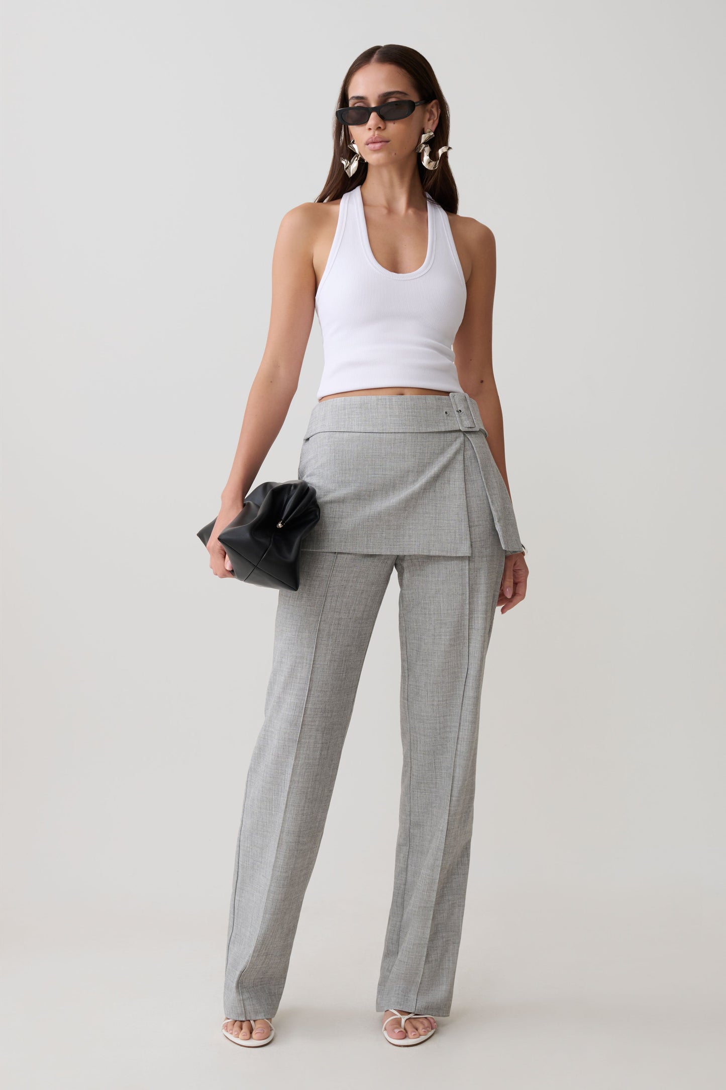 Woman wearing a white tank top and gray wrap skirt straight leg pants.