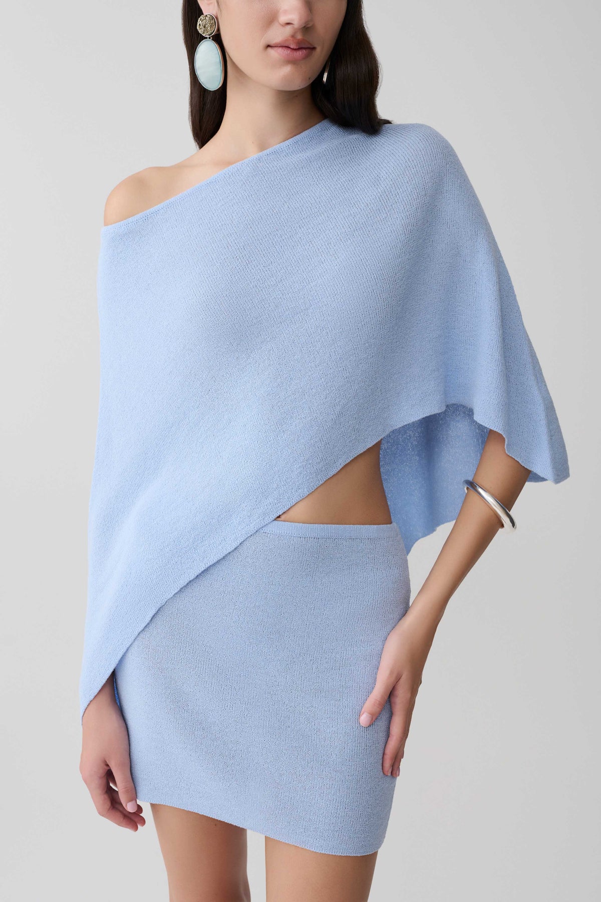 Woman wearing a light blue one shoulder knit cape top with matching skirt