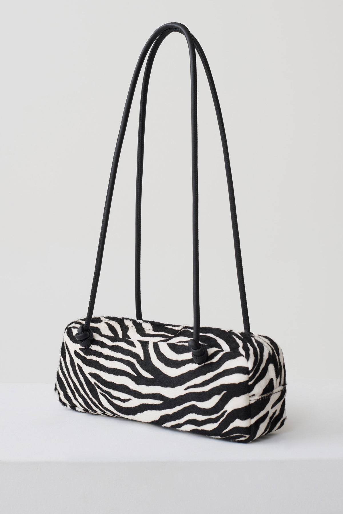 A zebra-print cylindrical shoulder bag with black double shoulder straps, displayed on a clean white studio background.