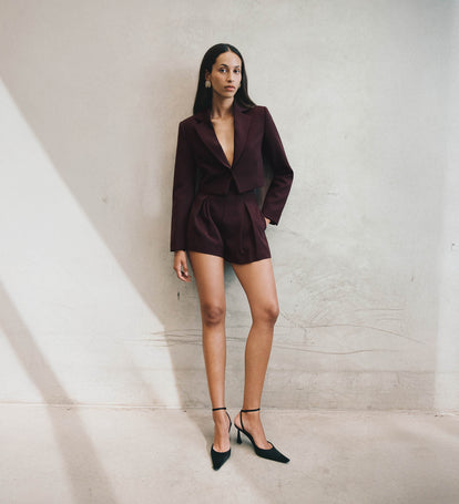 Woman wearing a burgundy suit against a neutral wall.