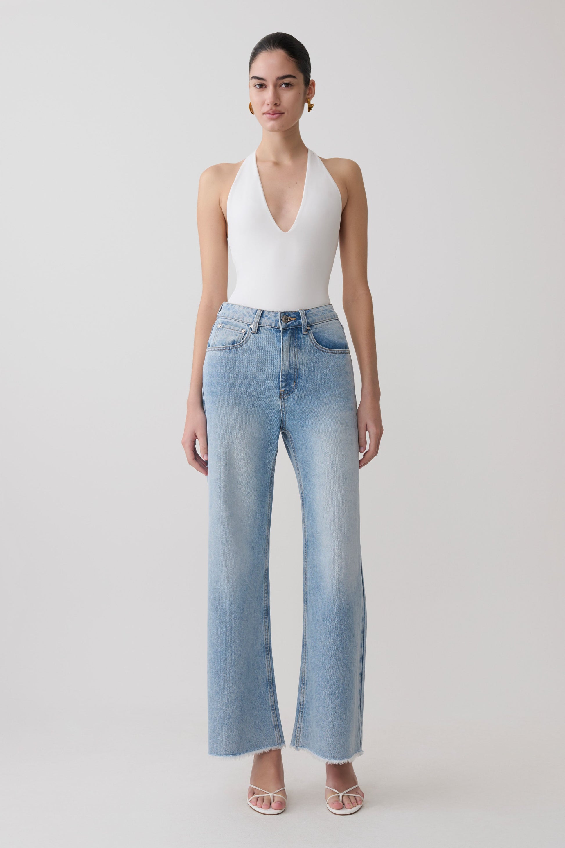Woman wearing a white slinky halter bodysuit with blue jeans.