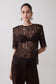 Woman wearing a dark brown shoulder pad short sleeve lace top.