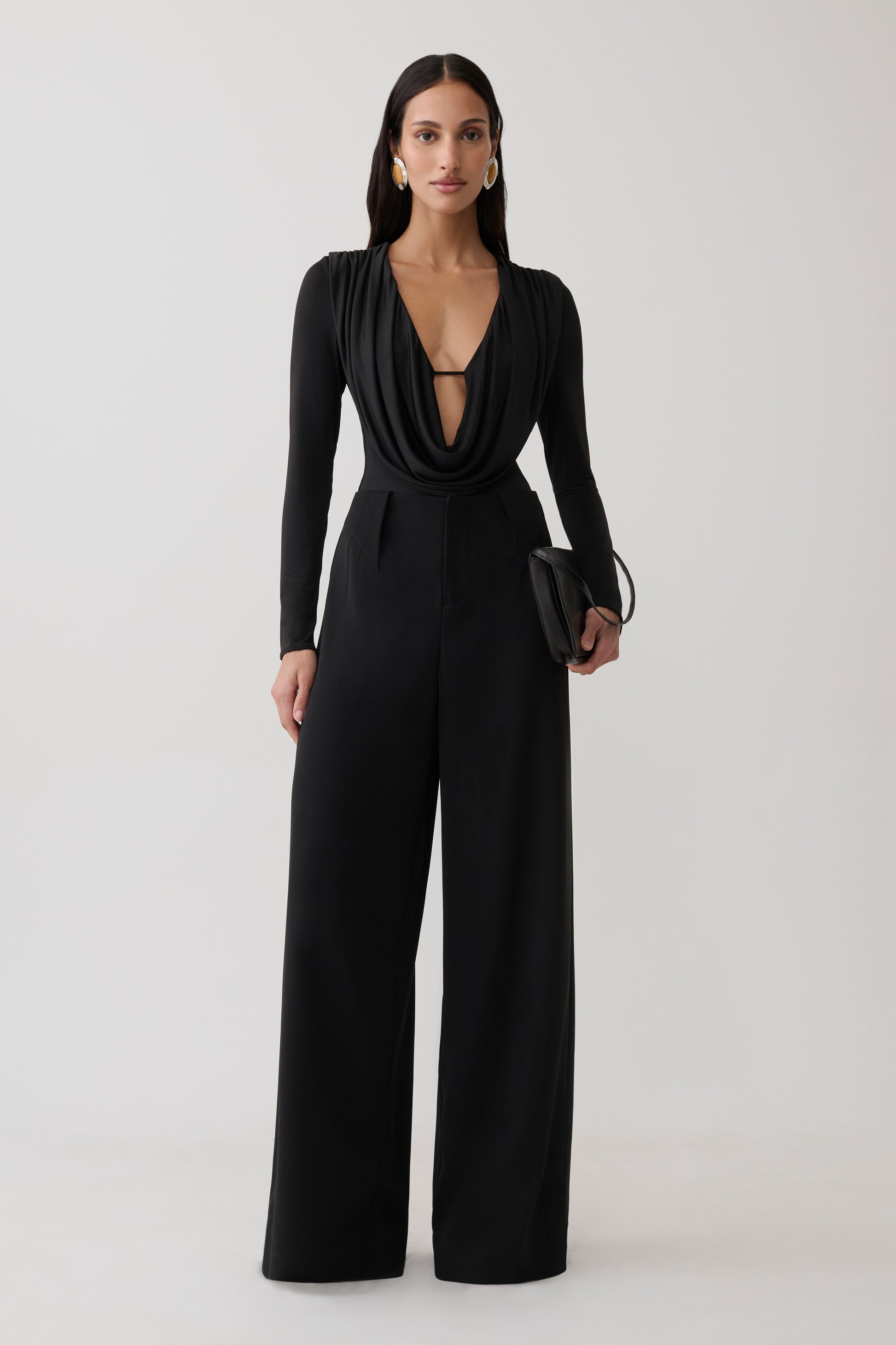 Woman wearing black cowl long sleeve slinky bodysuit, with black pants.
