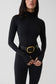 A model wearing a black long-sleeve mock-neck bodysuit with a wide black belt featuring a prominent gold buckle, set against a plain light gray studio background.
