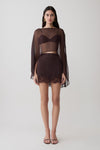 Woman wearing brown bralette with chiffon cape with matching lace and satin mini skirt.