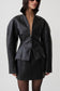 A model wearing a black textured faux-leather jacket with a high collar and a matching black mini skirt, photographed against a light gray studio background.