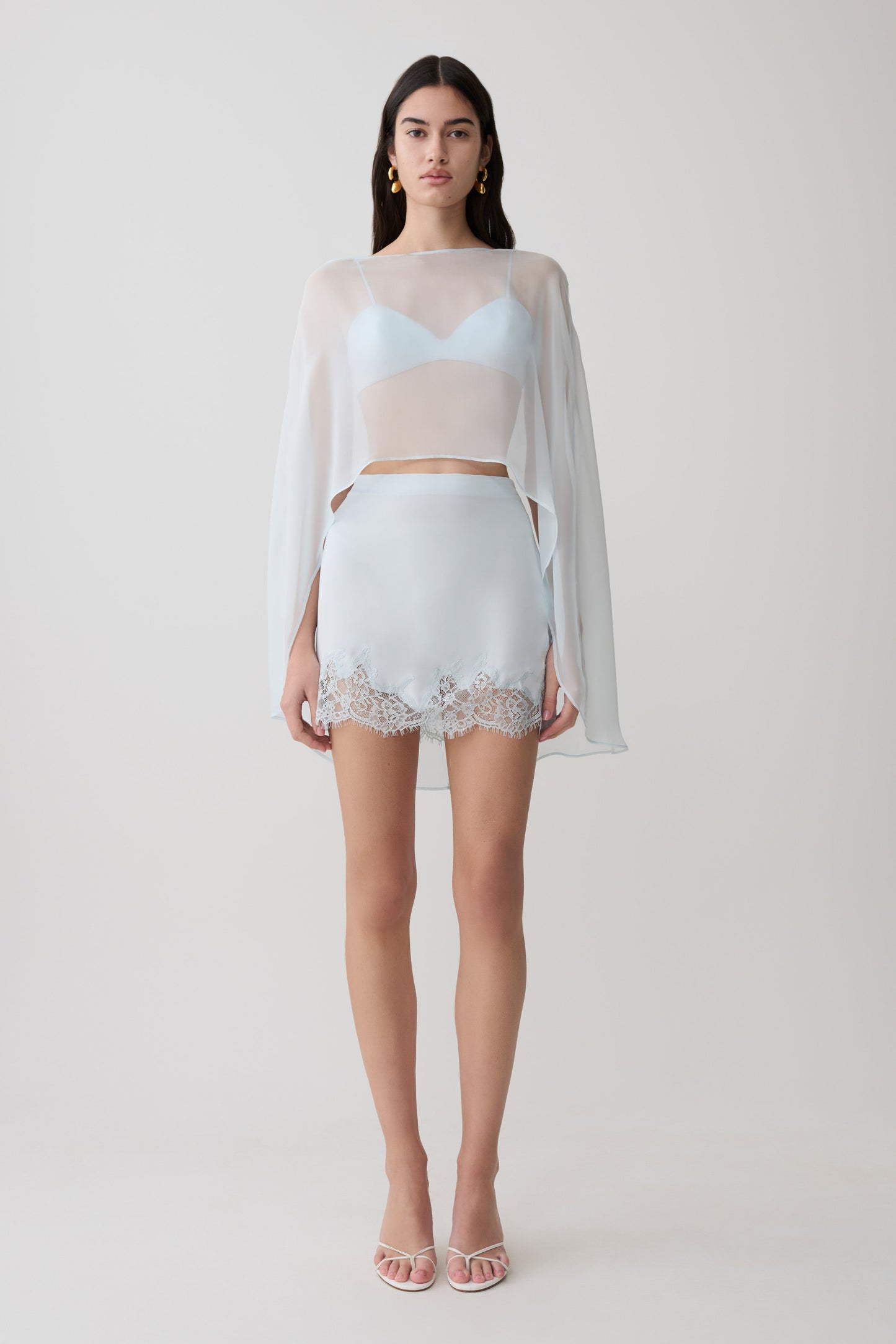 Woman wearing light blue bralette with chiffon cape with matching lace and satin mini skirt.