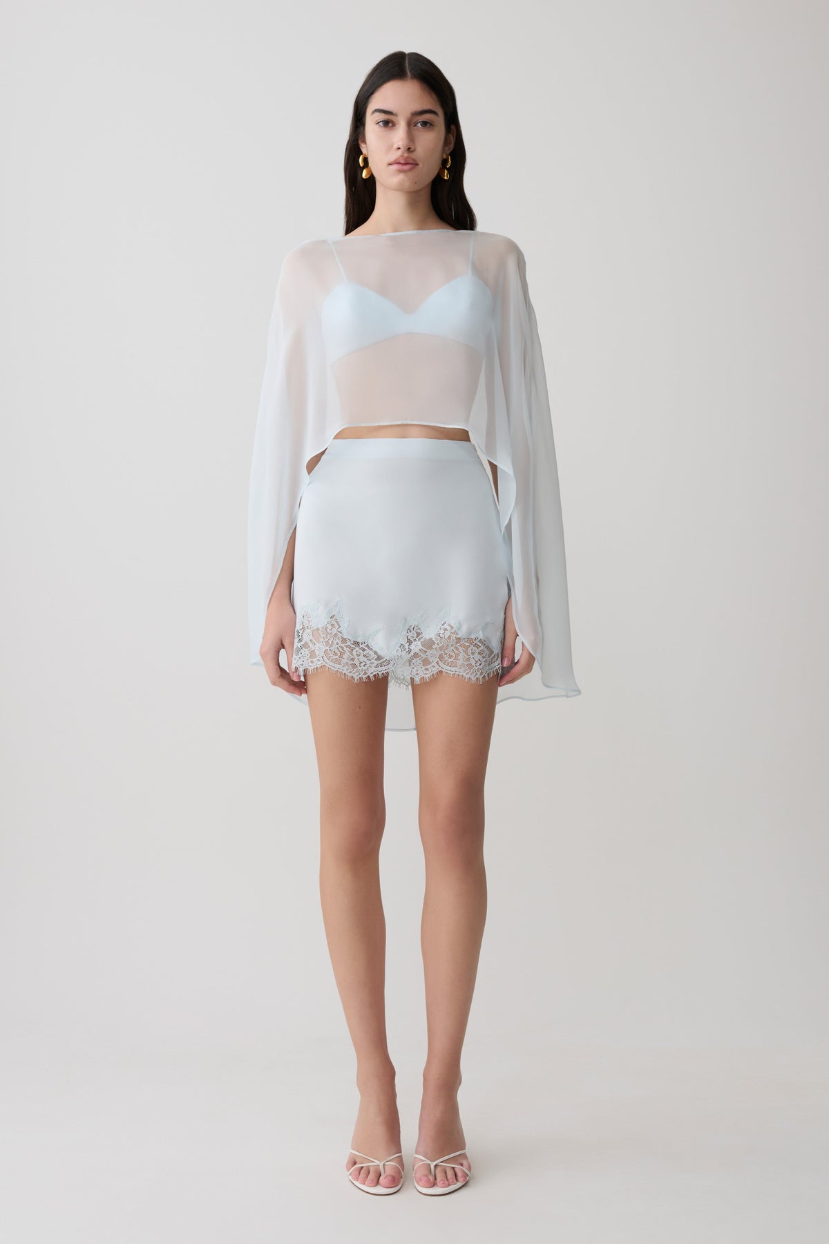 Woman wearing light blue bralette with chiffon cape with matching lace and satin mini skirt.