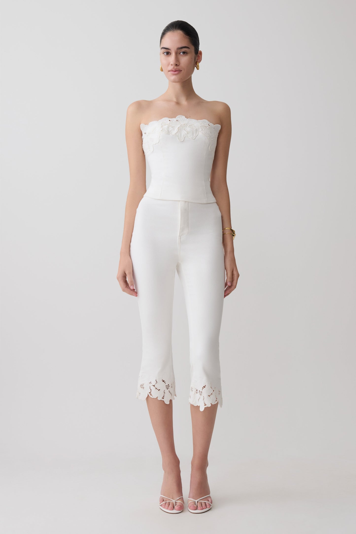 Woman wearing a white embroidery strapless denim top and white flower embroidery denim capris.