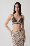Woman wearing a nude lace sleeveless crop top.