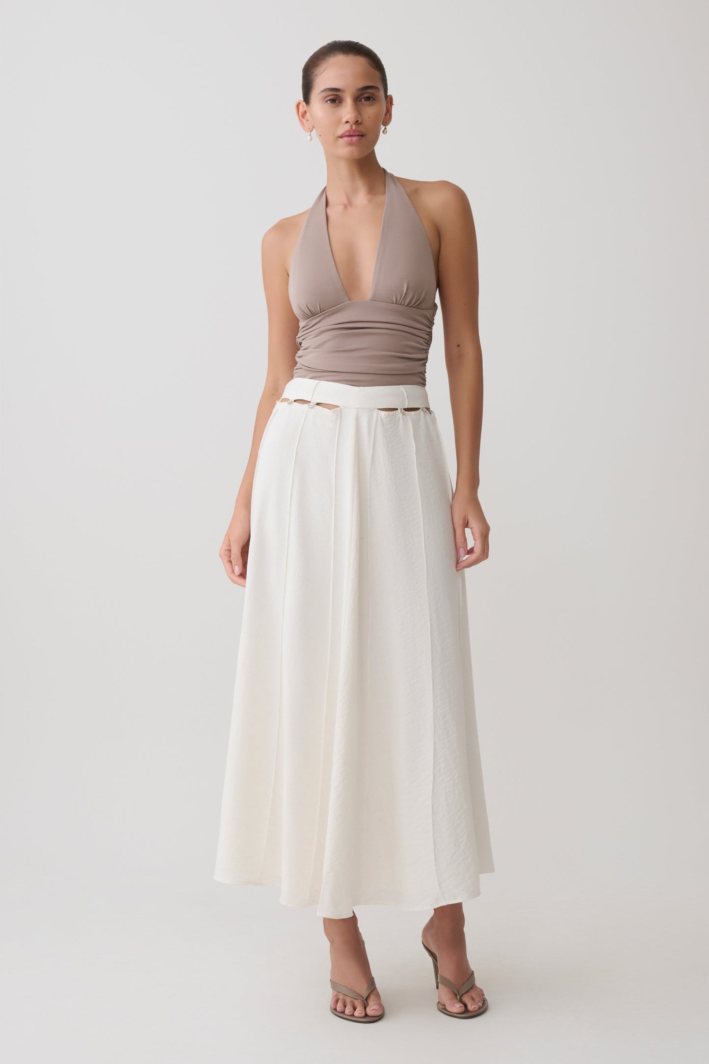 Woman wearing a brown halter top and peral button white midi skirt.
