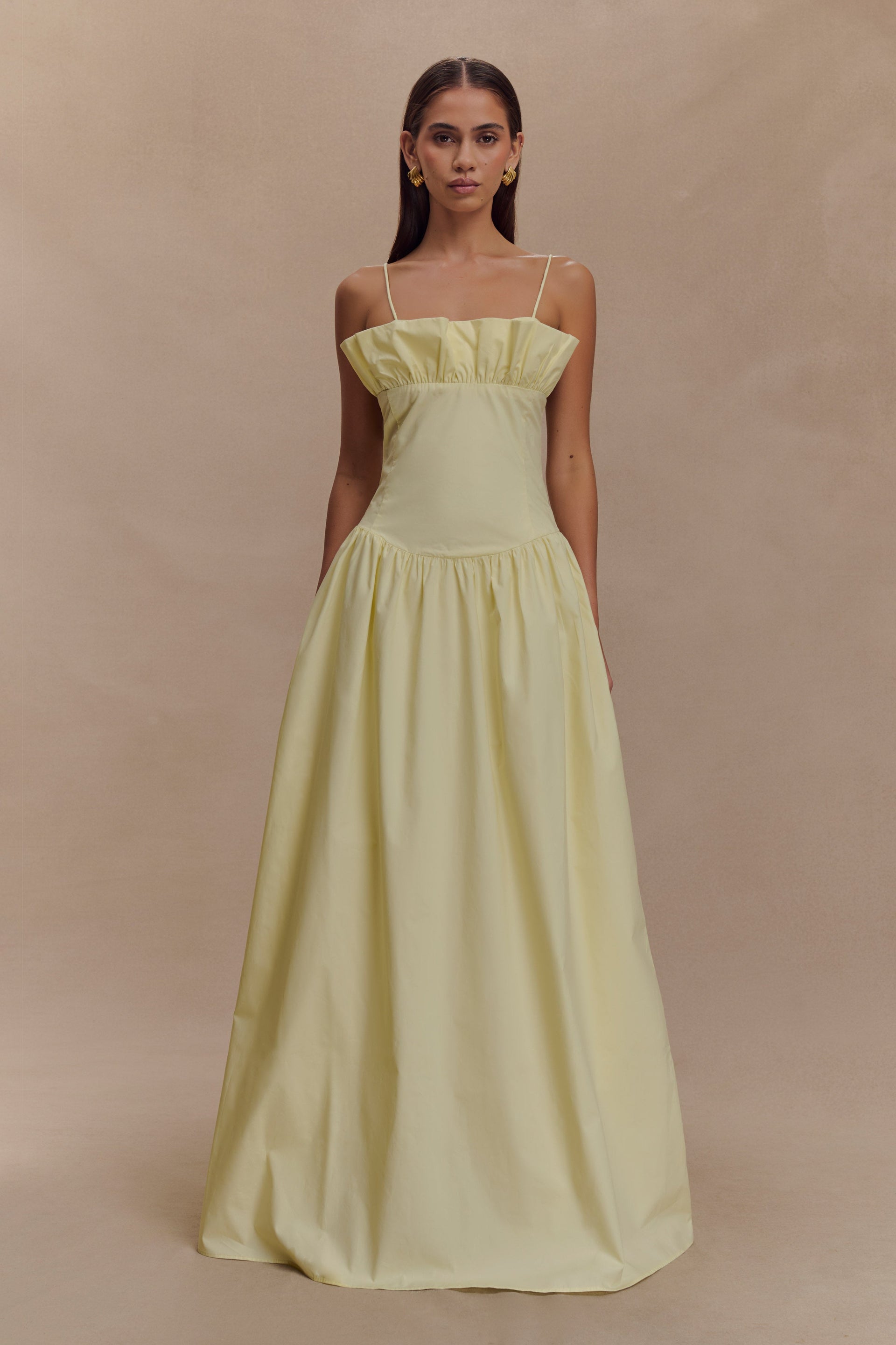 A model wearing a lemon yellow maxi dress with a frill-gathered neckline and slender spaghetti straps.