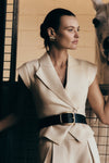 A model wearing a beige short-sleeve linen top with an asymmetric lapel neckline and a button closure. The top is paired with a mid-rise wide-leg linen pant.