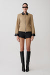 Person wearing a beige jacket with black accents, black shorts, and black knee-high boots on a white background.