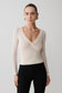 Woman wearing a cream long-sleeve top with a V-neckline on a plain background