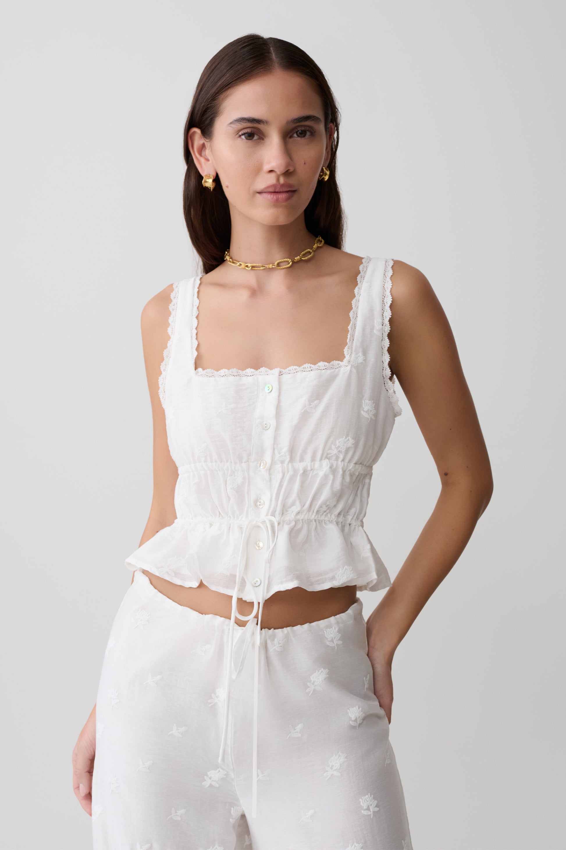 Woman wearing a white embroidered sleeveless top.