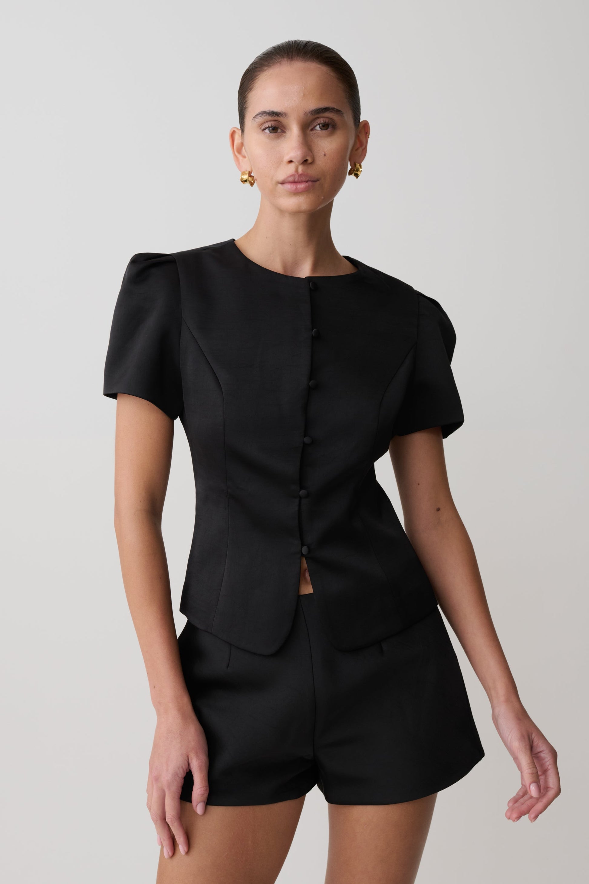 Woman wearing a black outfit with puffed sleeves on a plain background