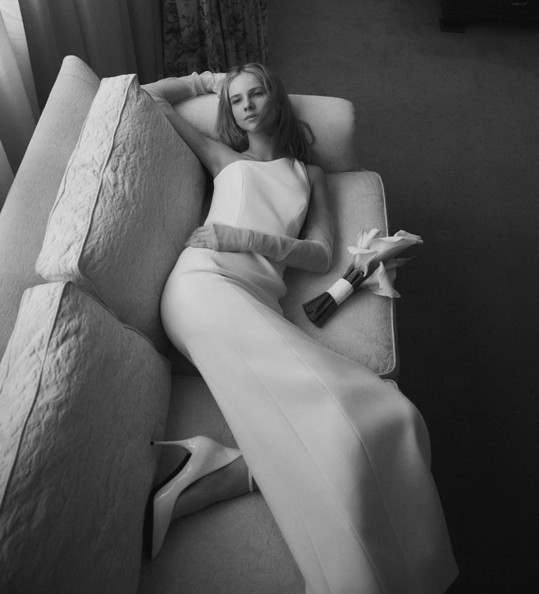 Woman in a white dress lying on a couch with a bouquet of flowers.