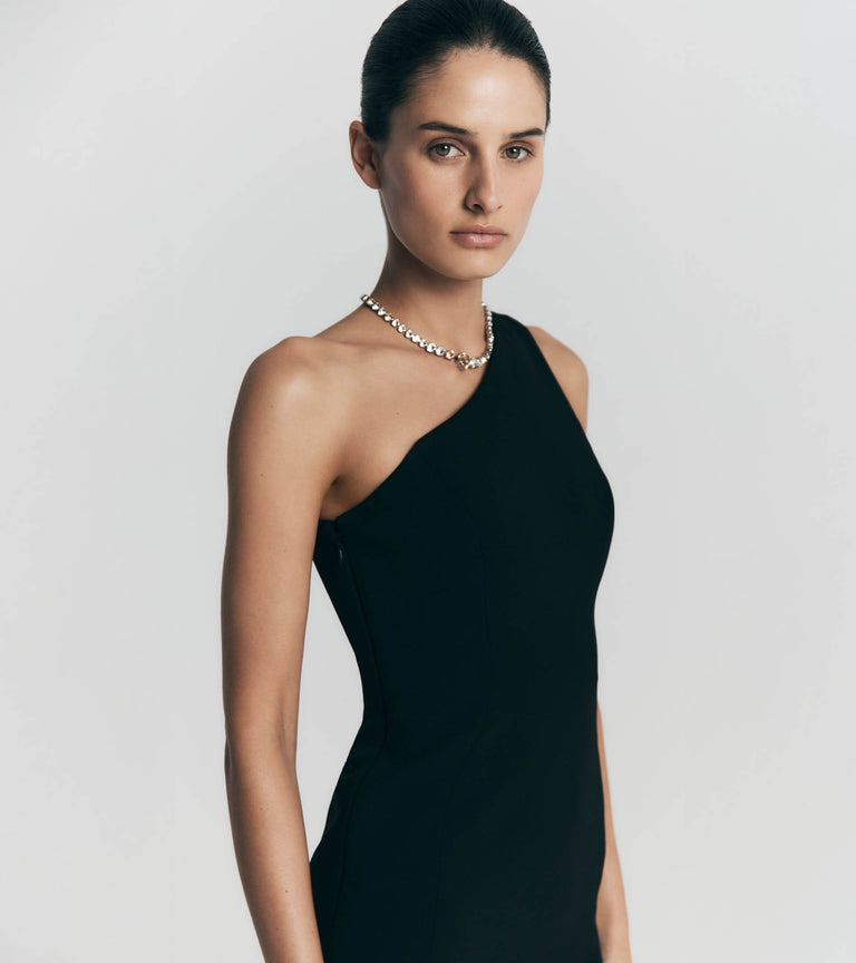 Woman wearing a black one-shoulder dress with a plain background.