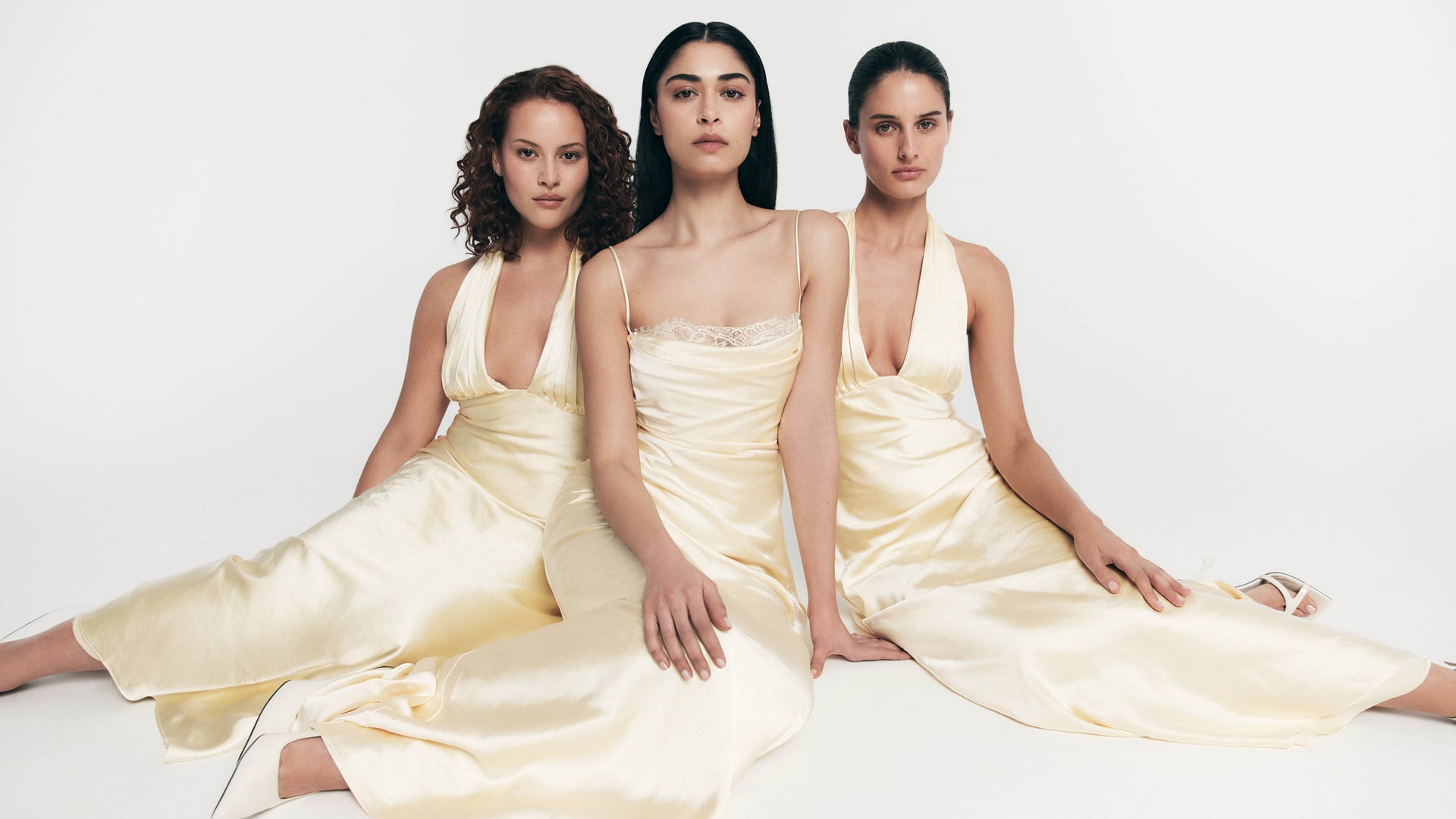 Three women in yellow dresses sitting side by side on a white background.