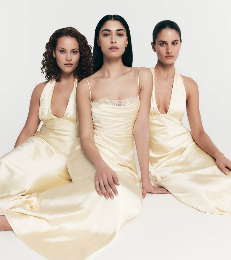 Three women in yellow dresses sitting side by side on a white background.