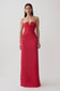 A woman modeling a strapless red floor-length gown with a sweetheart neckline, ruched bodice, and gathered waist details, photographed against a plain light gray studio background.