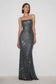 A woman modeling a floor-length, spaghetti-strap evening gown covered in dark gray sequins against a plain light gray studio background.