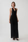 A woman modeling a sleeveless black halter-neck maxi dress with a subtle dotted pattern, photographed against a plain light gray studio background.