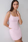 A woman modeling a light pink sleeveless mini dress with a structured bodice, square neckline, and side cutouts against a plain light gray background.
