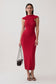 A woman modeling a fitted sleeveless red midi dress with a high mock neck and cap shoulders, holding a small black handbag against a plain light gray studio background.