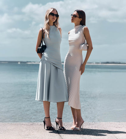 Two women at the pier. One in blue high neck midi dress, the other in a while high neck midi dress. 