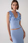 A woman modeling a light blue ribbed knit two-piece set featuring a ruffled halter-style top with a low waist cutout and a matching high-waisted skirt, against a plain light gray studio background.