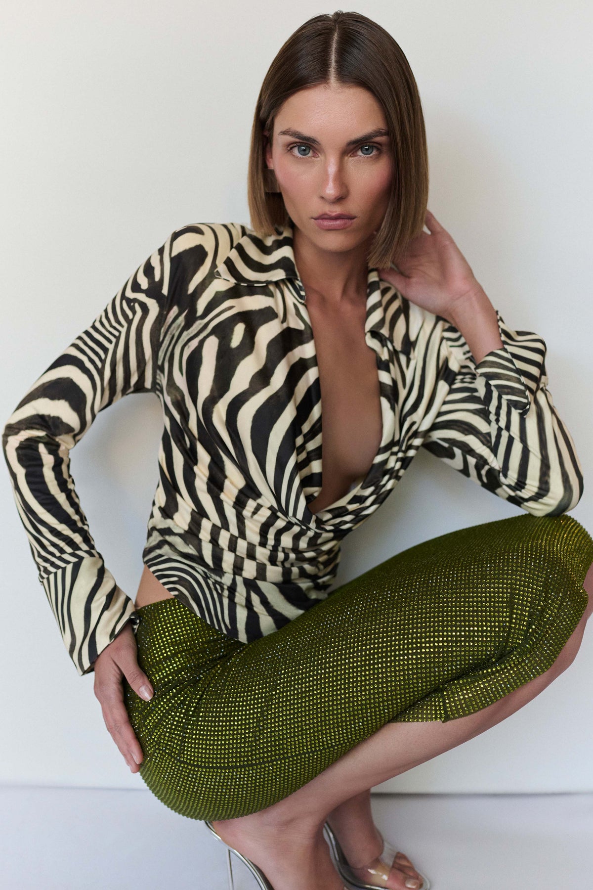 A model wearing a black and beige zebra-print long-sleeve top and textured olive green pants, posing against a plain white wall.