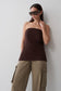 A woman wearing a dark brown strapless tube top and khaki cargo pants, standing against a light gray wall.
