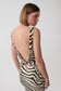 A woman shown from the back wearing a zebra-print dress with a deep open back and tie detail, photographed against a light gray studio background.